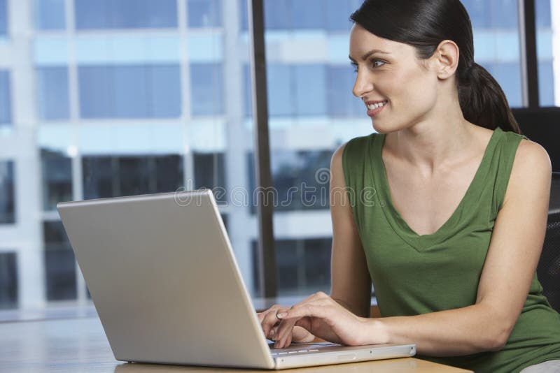 Mulher que usa o portátil na mesa de escritório imagem de stock royalty free Mulher que usa o portátil na mesa de escritório imagem de stock royalty free