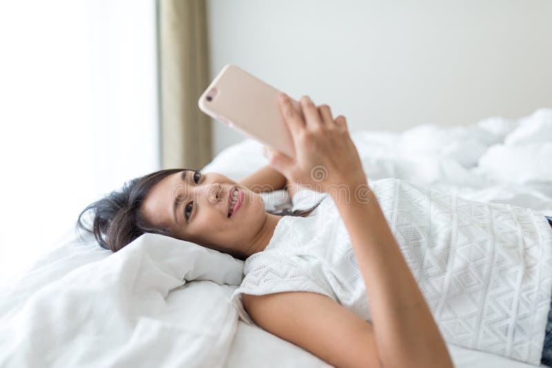 A mulher que usa o telefone celular e estabelece na cama fotografia de stock A mulher que usa o telefone celular e estabelece na cama fotografia de stock