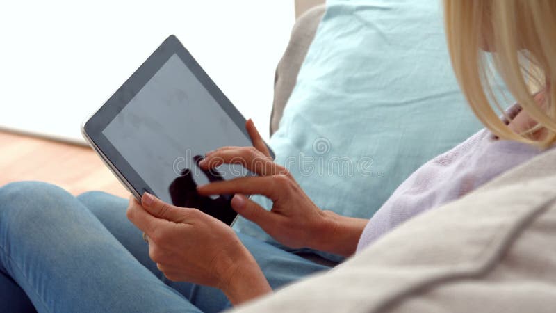 Mulher que usa a tabuleta no sofá filme