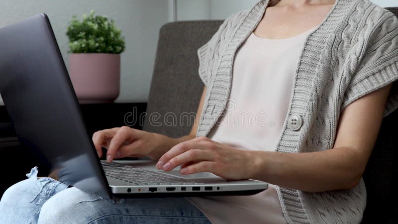 Mulher sentada no sofá em casa e digitando no laptop