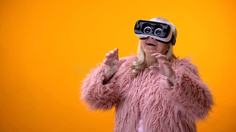 Mulher superior positiva no revestimento engraçado e nos auriculares de VR que jogam a tecnologia do jogo de vídeo fotos de stock royalty free Mulher superior positiva no revestimento engraçado e nos auriculares de VR que jogam a tecnologia do jogo de vídeo fotos de stock royalty free
