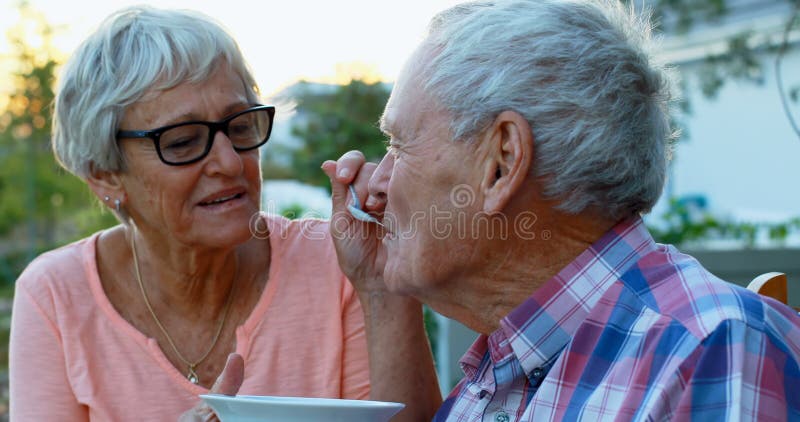 Mulher superior que alimenta o homem superior no quintal 4k