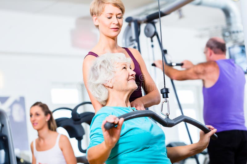 Mulher superior que faz o treinamento traseiro com o instrutor no gym foto de stock Mulher superior que faz o treinamento traseiro com o instrutor no gym foto de stock