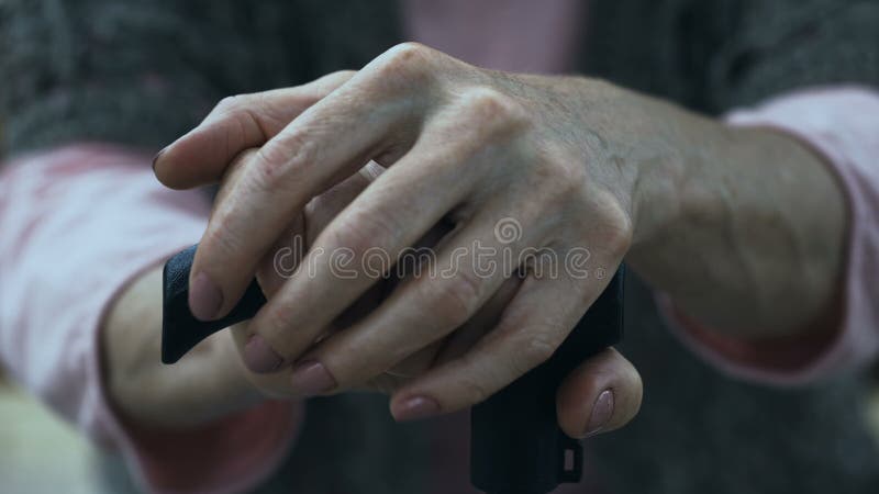 Mulher superior que inclina-se na vara de passeio, sentando-se no banco no parque do lar de idosos