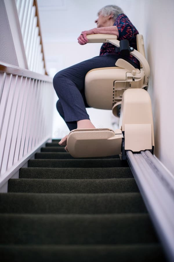 Mulher superior que senta-se no elevador da escada em casa para ajudar a mobilidade