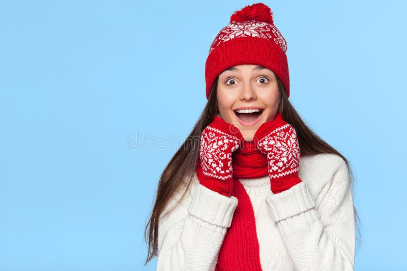 Mulher surpreendida feliz que olha lateralmente no excitamento Menina do Natal que veste o chapéu feito malha e os mitenes mornos