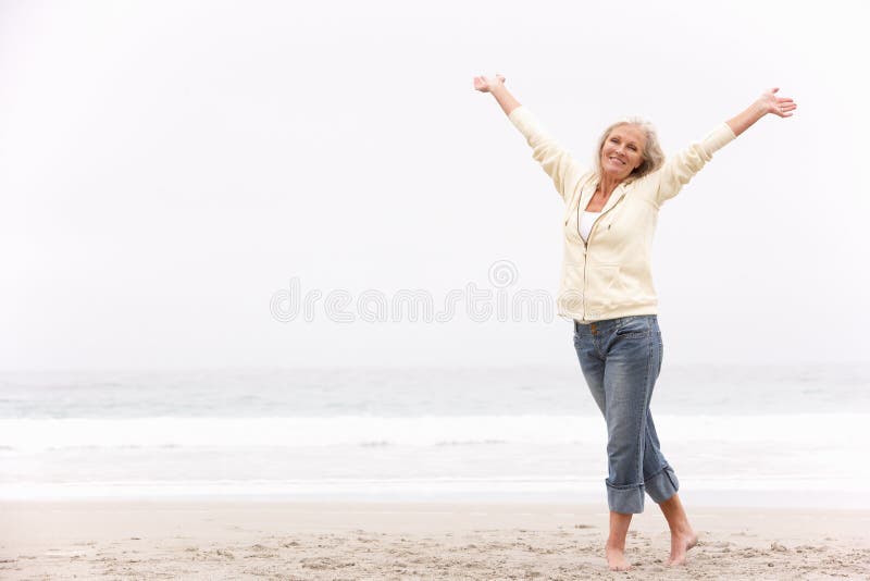 A mulher sênior com braços Outstretched na praia