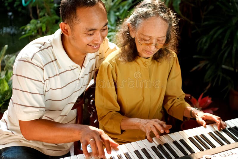 Mulher sênior étnica e homem novo que jogam o piano fotografia de stock Mulher sênior étnica e homem novo que jogam o piano fotografia de stock