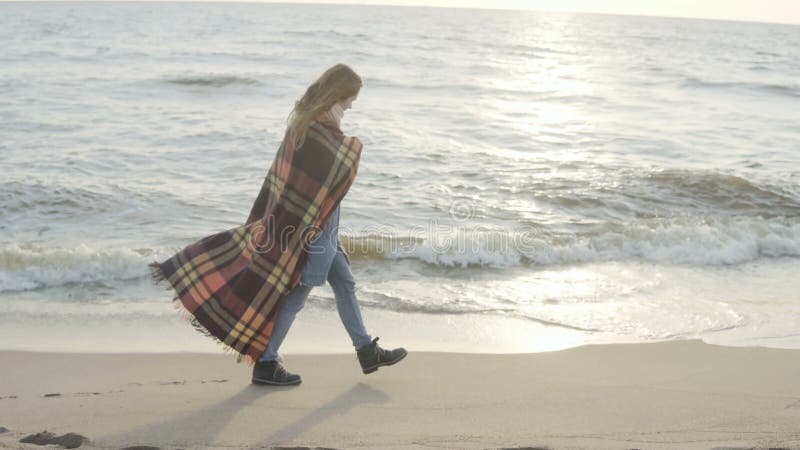 Mulher só que anda no Sandy Beach com manta Tempo de gasto fêmea novo na costa do mar no dia frio