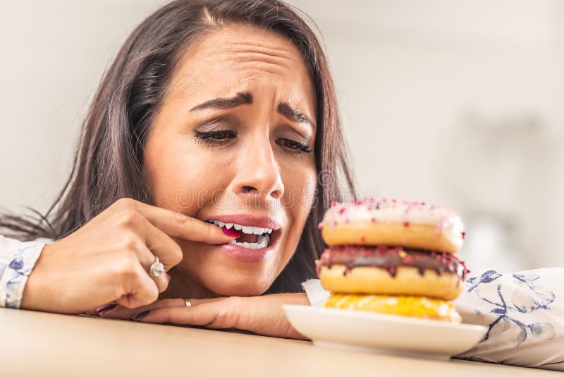 Mulher tentando desesperadamente resistir a donuts, mordendo o dedo