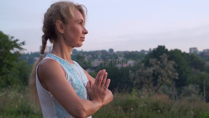 A mulher Yogin olha o lado da aumentação Sun e guarda as mãos na boa vinda do ` s de Namaste no parque da cidade