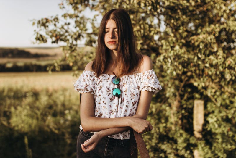 Mulher à moda do moderno que relaxa na noite sob a luz solar no summ imagem de stock Mulher à moda do moderno que relaxa na noite sob a luz solar no summ imagem de stock