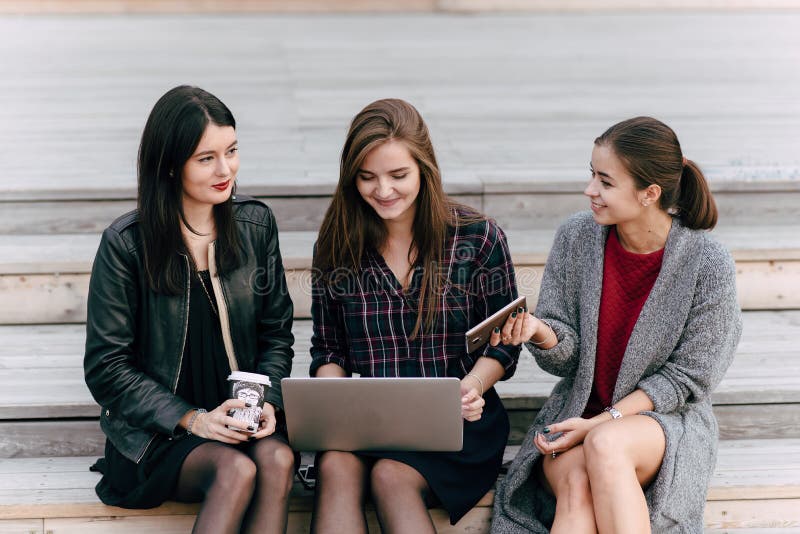 Mulheres alegres novas da árvore com olhar elegante que falam entre se quando seu amigo que trabalha no rede-livro portátil imagem de stock Mulheres alegres novas da árvore com olhar elegante que falam entre se quando seu amigo que trabalha no rede-livro portátil imagem de stock