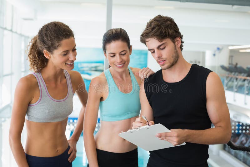 Mulheres aptas com o instrutor que toma notas e que sorri na câmera fotografia de stock Mulheres aptas com o instrutor que toma notas e que sorri na câmera fotografia de stock