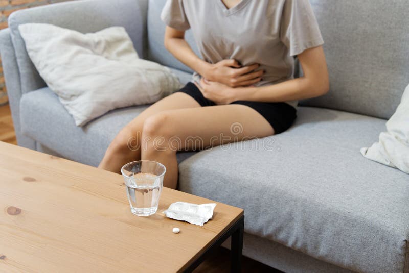Mulheres asiáticas novas no sofrimento do sofá da dor de estômago e para ter alguma febre devido à menstruação imagem de stock Mulheres asiáticas novas no sofrimento do sofá da dor de estômago e para ter alguma febre devido à menstruação imagem de stock