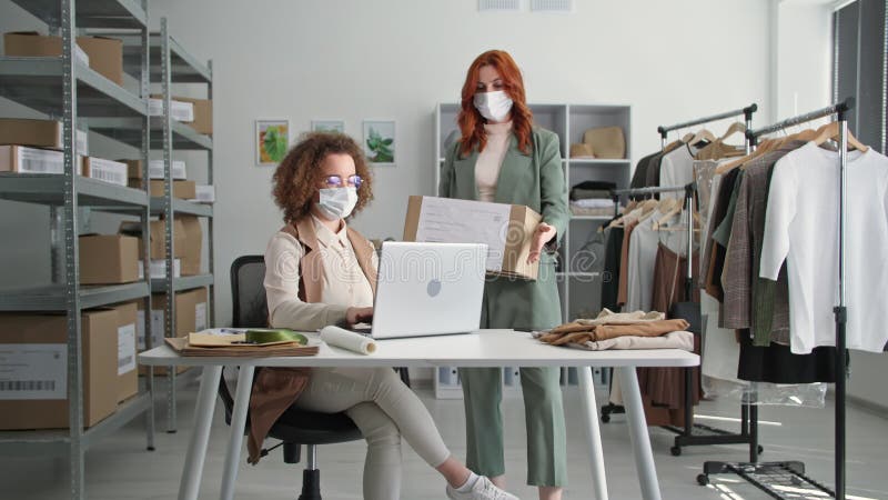 Mulheres empresárias jovens usando máscara médica face à entrega de roupas a clientes em uma loja online