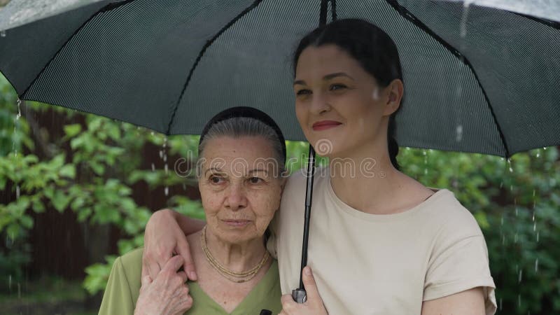 Mulheres idosas e jovens sob guarda-chuva na chuva video estoque