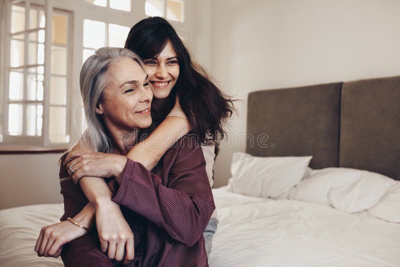 Mulheres idosas que sentam-se na cama com sua filha que guarda suas mãos Mãe e filha de sorriso que sentam-se em casa passando o fotografia de stock royalty free Mulheres idosas que sentam-se na cama com sua filha que guarda suas mãos Mãe e filha de sorriso que sentam-se em casa passando o fotografia de stock royalty free