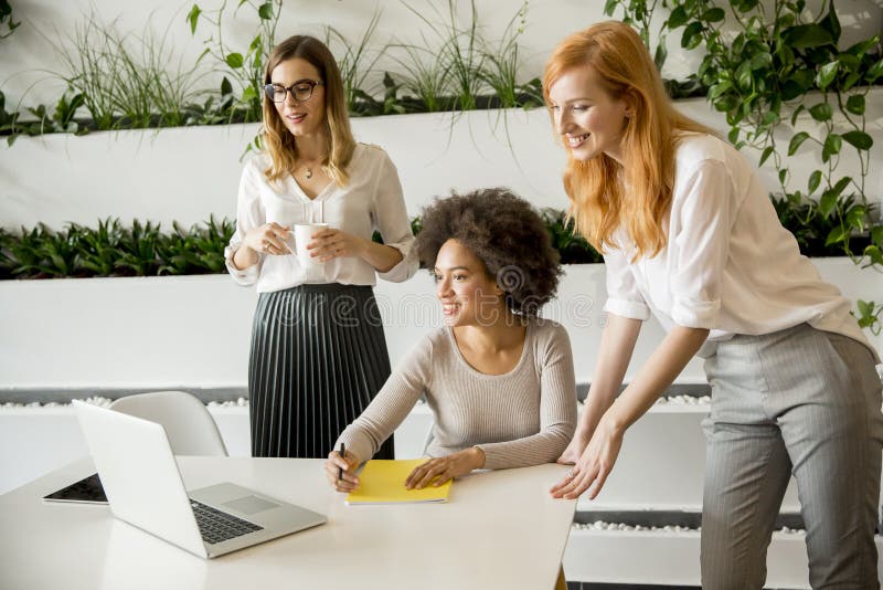 Mulheres multirraciais profissionais alegres que trabalham no escritório moderno imagem de stock Mulheres multirraciais profissionais alegres que trabalham no escritório moderno imagem de stock