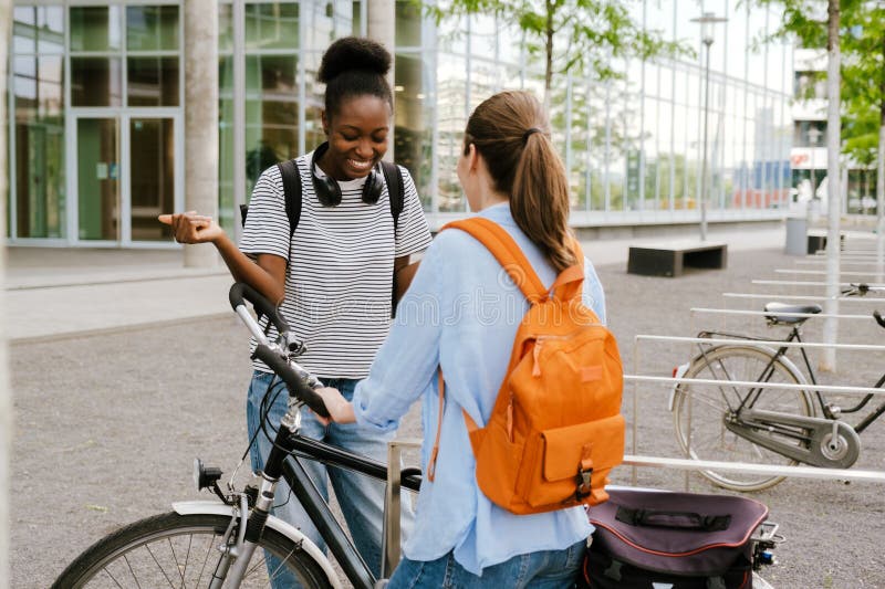 Mulheres multirraciais rindo de bicicleta em pé na rua fotos de stock royalty free