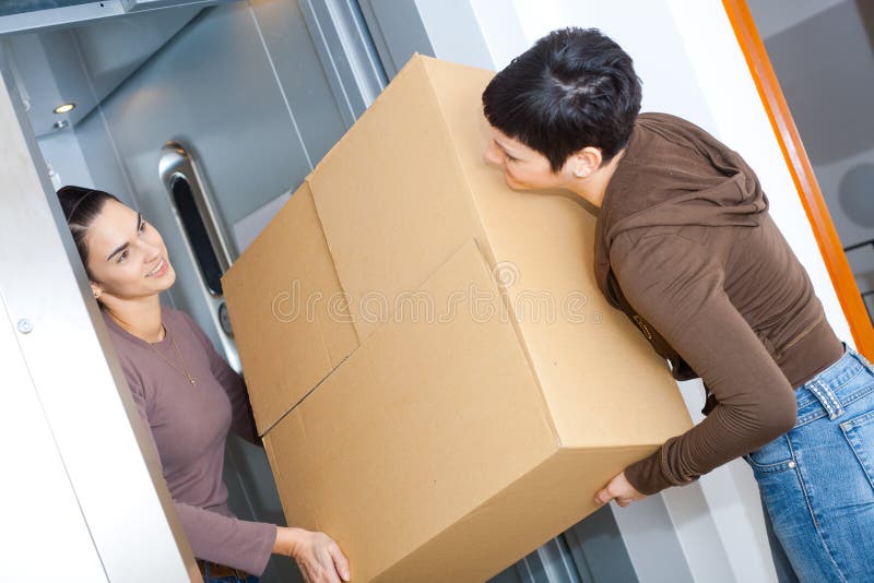 Two happy women moving cardboard box with elevator, smiling. Two happy women moving cardboard box with elevator, smiling.