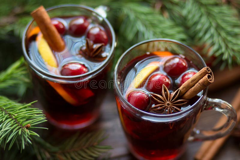 Mulled wine in glass mug with berries, cinnamon sticks and star anise on brown wood table