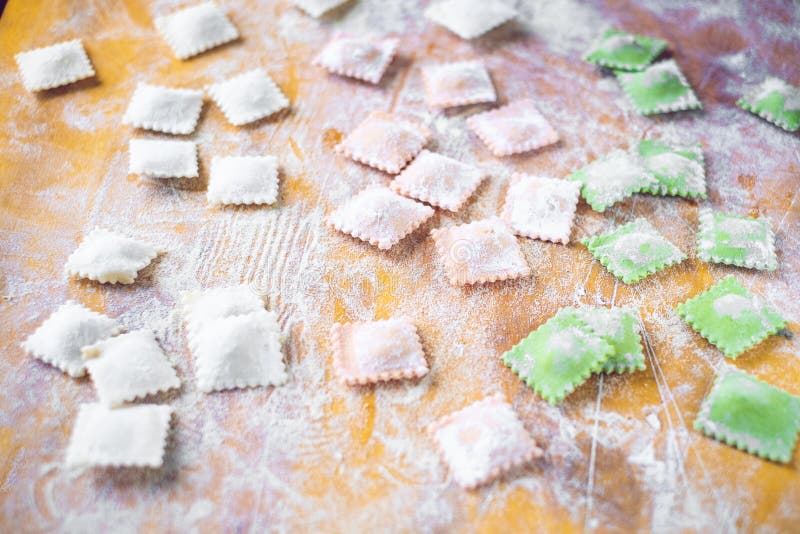 Multi-colored uncooked ravioli on a cutting board, sprinkled with flour, handmade, on a wooden table. cooking process. Multi-colored uncooked ravioli on a cutting board, sprinkled with flour, handmade, on a wooden table. cooking process