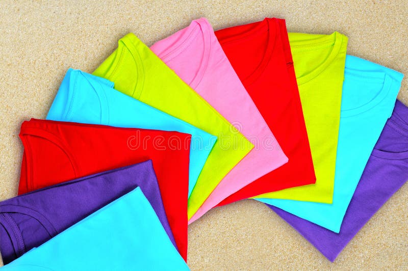 Multi-colored vrouwen` s t-shirts liggen op beige achtergrond stock afbeelding Multi-colored vrouwen` s t-shirts liggen op beige achtergrond stock afbeelding