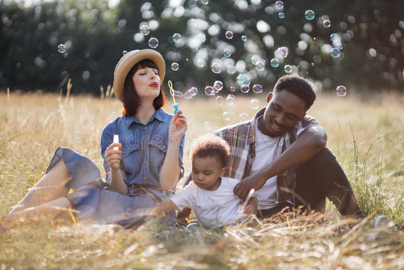 Multi ethnic parents with son blowing soap bubbles outdoors