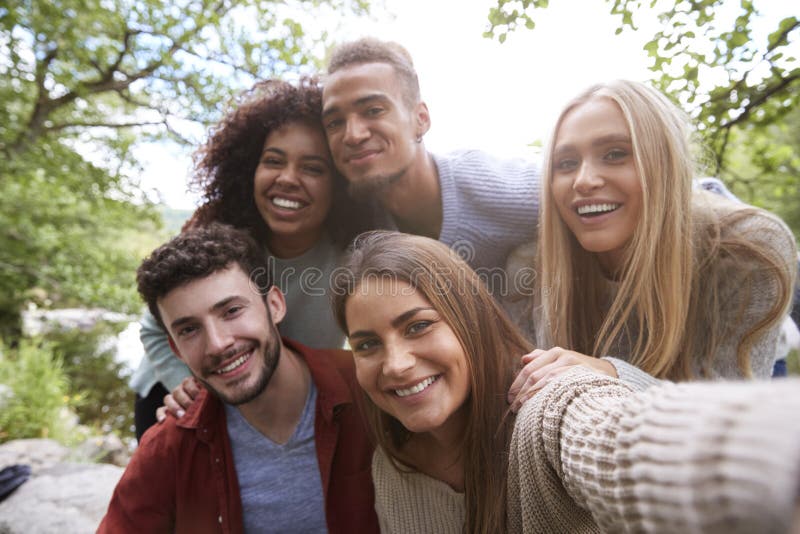 Multi Ethnie von fünf jungen erwachsenen Freunden werfen zur Kamera beim Nehmen eines selfie während eines Bruches in einer Wande lizenzfreie stockbilder