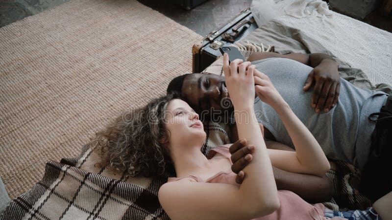 Multi-etnisch paar die op bed liggen Man en vrouw die, gebruikend een smartphone lachen Het mannetje en het wijfje brengen samen stock afbeeldingen Multi-etnisch paar die op bed liggen Man en vrouw die, gebruikend een smartphone lachen Het mannetje en het wijfje brengen samen stock afbeeldingen