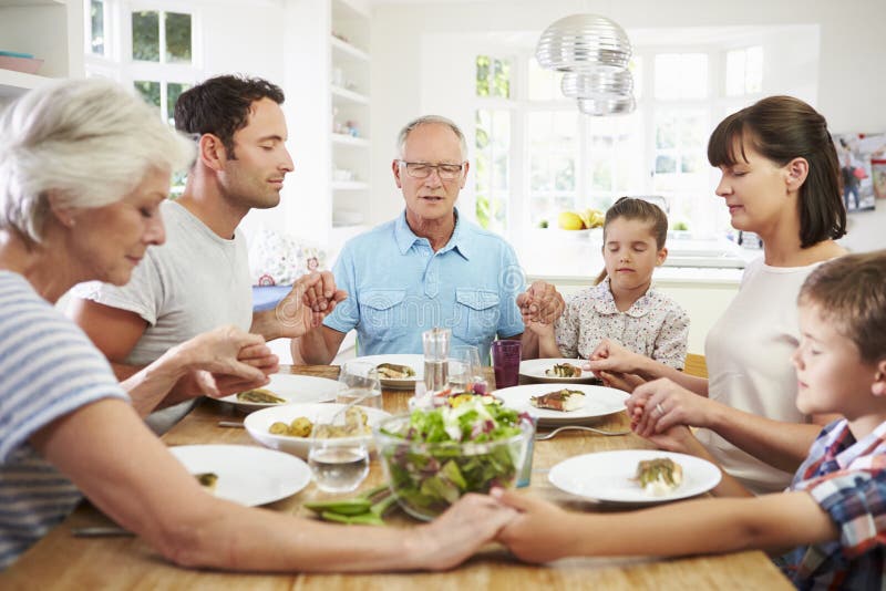 Multi famiglia della generazione che prega prima del pasto a casa fotografia stock Multi famiglia della generazione che prega prima del pasto a casa fotografia stock