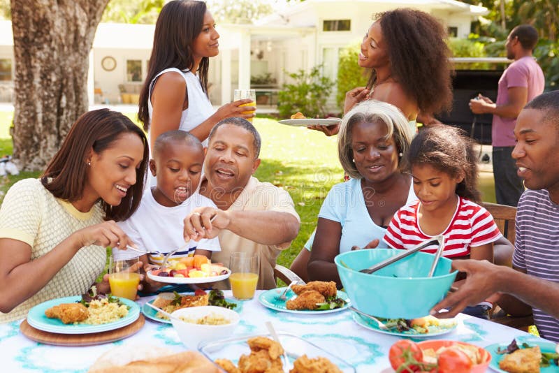 Multi família da geração que aprecia a refeição no jardim junto