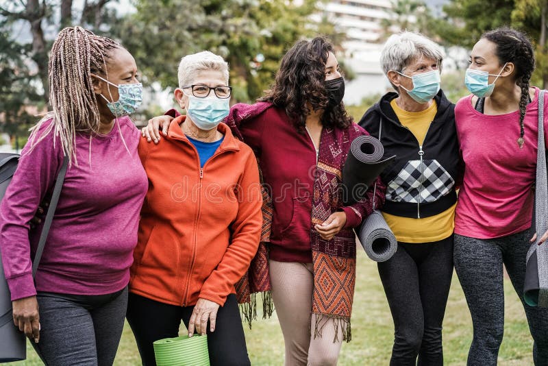 Multi generational women having fun before yoga class wearing safety masks at park outdoor - Main focus on right girl face