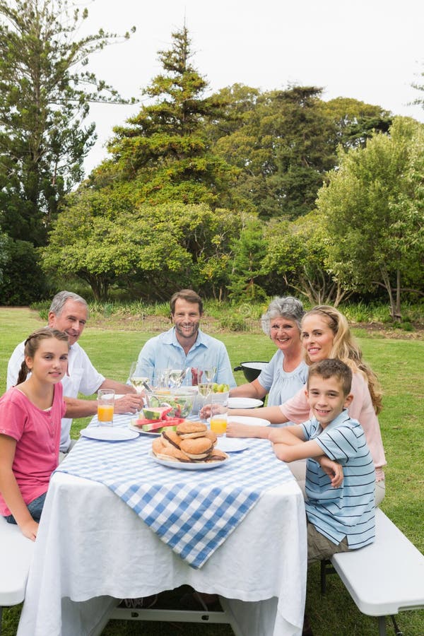 Multi Generationsfamilie am Picknicktisch, der draußen zu Abend isst lizenzfreie stockbilder Multi Generationsfamilie am Picknicktisch, der draußen zu Abend isst lizenzfreie stockbilder