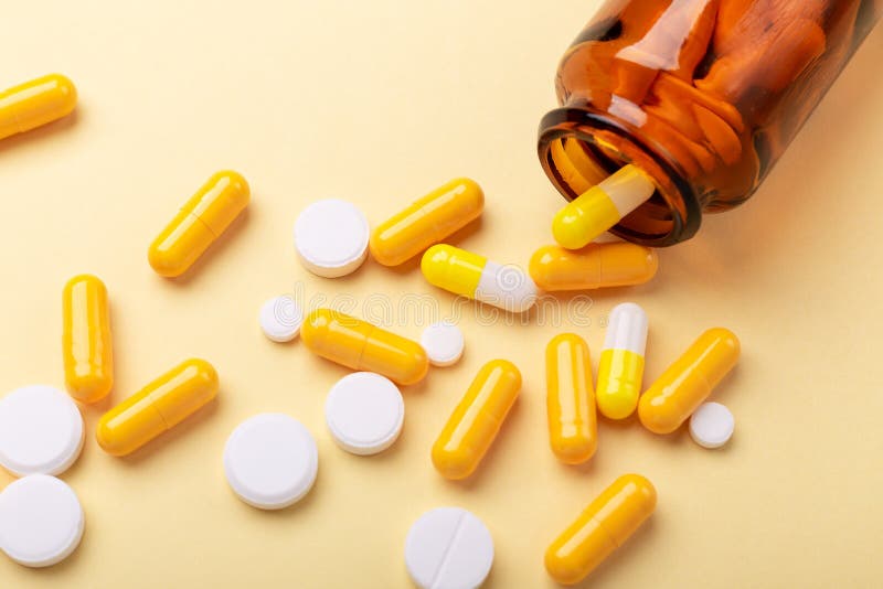 Multicolor tablets and pills capsules from glass bottle on yellow background Close-up