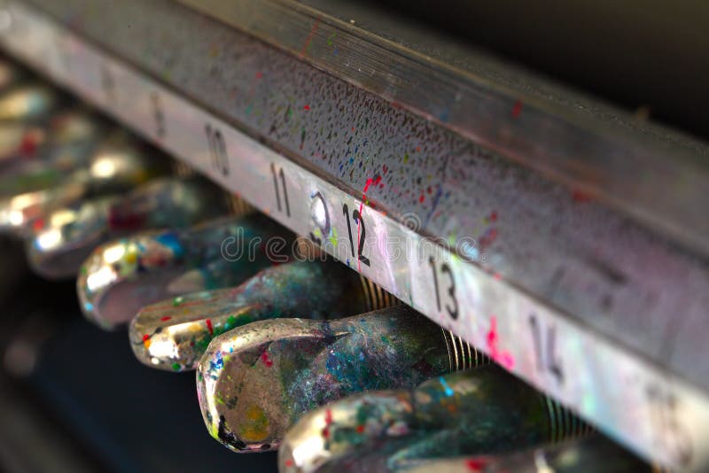 Multicolored drops of paint on the tuners of the old printing press. Close-up of a fragment of an offset machine stock photography