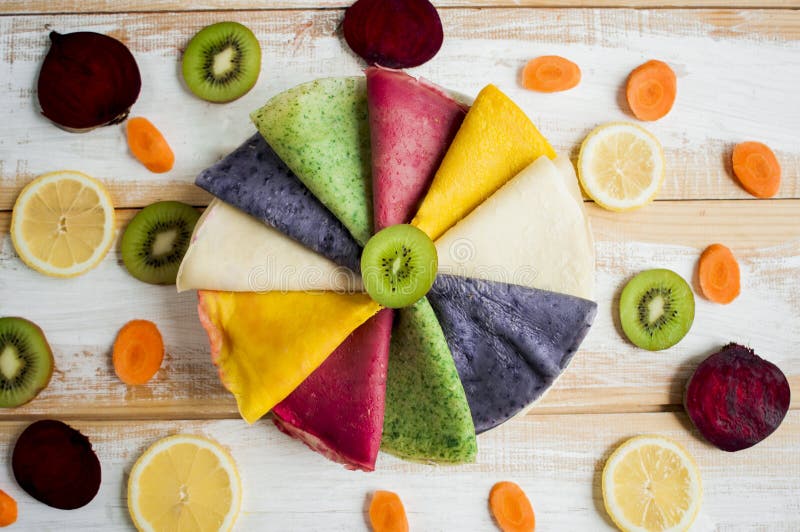 Multicolored pancakes lined on plate in a circle and decorated with pieces of beetroot, lemon, carrot, kiwis, stock photo Multicolored pancakes lined on plate in a circle and decorated with pieces of beetroot, lemon, carrot, kiwis, stock photo