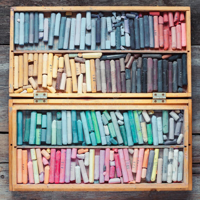 Multicolored pastel crayons in wooden artist box on table.