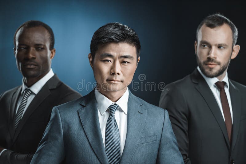 Selective focus of multicultural group of businessmen in suits looking at asian colleague. Isolated on black royalty free stock image Selective focus of multicultural group of businessmen in suits looking at asian colleague. Isolated on black royalty free stock image