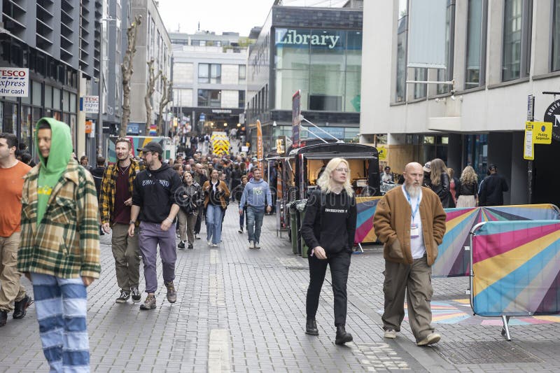 Multidão de pessoas diversas a caminhar numa rua pavimentada da cidade com bancas de comida e edifícios foto de stock royalty free
