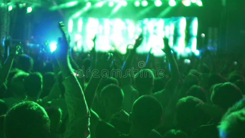 Multidão enorme de jovens felizes que dançam e que saltam à música no concerto fresco