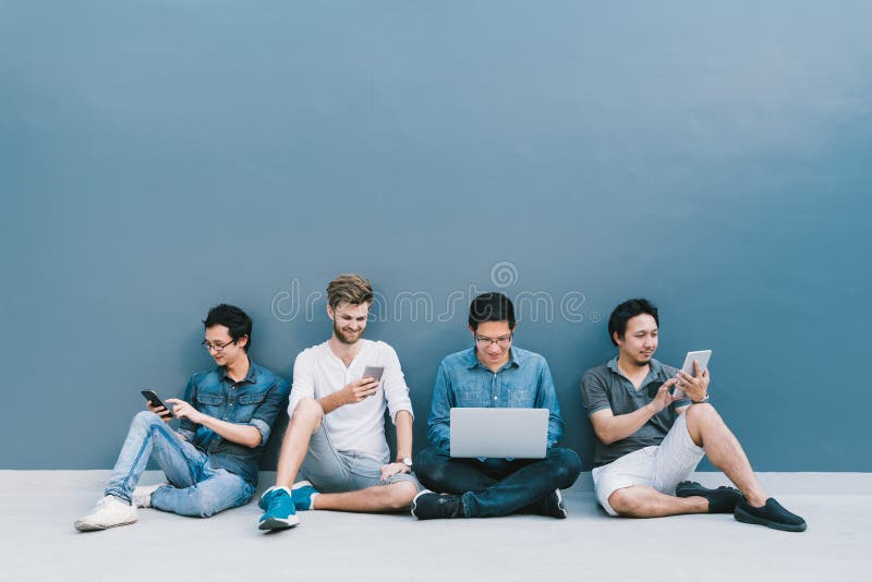 Multiethnic group of four men using smartphone, laptop computer, digital tablet together with copy space on blue wall stock photos Multiethnic group of four men using smartphone, laptop computer, digital tablet together with copy space on blue wall stock photos