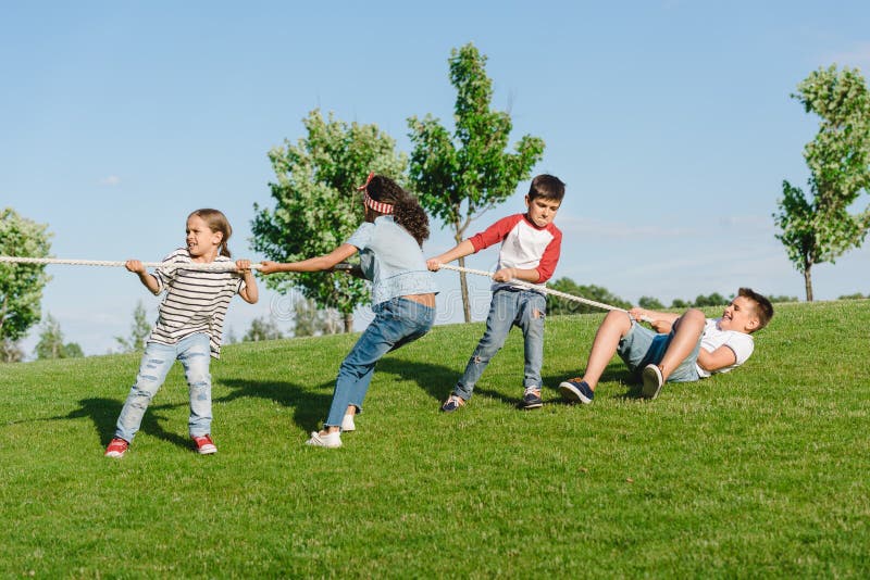 Multiethnic Kids Pulling Rope And Playing Tug Of War In Park Stock
