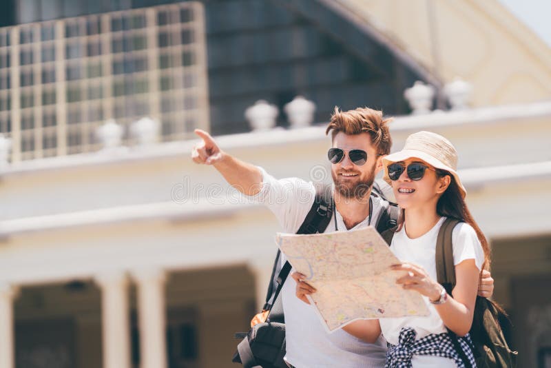 Multiethnic traveler couple using generic local map together on sunny day, men pointing toward copy space. Honeymoon trip, backpacker tourist, Asia tourism, or holiday vacation travel concept. Multiethnic traveler couple using generic local map together on sunny day, men pointing toward copy space. Honeymoon trip, backpacker tourist, Asia tourism, or holiday vacation travel concept