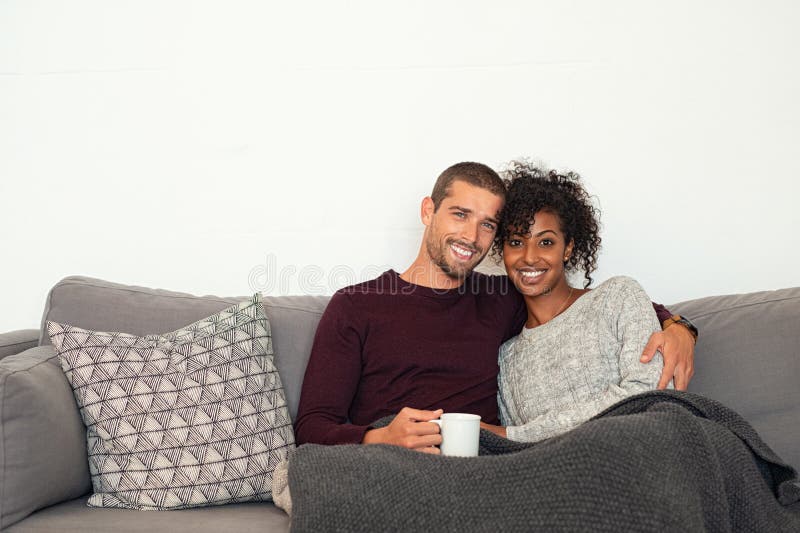 Multiethnische Paare, die auf dem Couchumarmen sitzen
