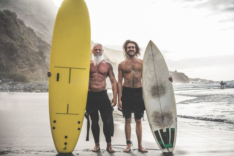 Multigeneration friends going to surf on tropical beach - Family people having fun doing extreme sport - Joyful elderly and