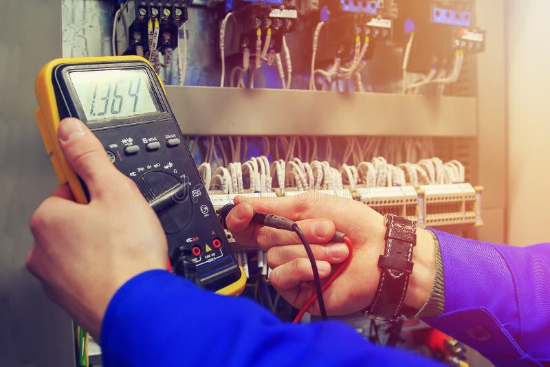 Multimeter in hands of electrician close-up against background of electrical wires and relays stock photo