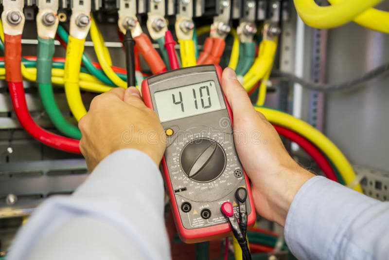 Multimeter in hands of electrician in power high voltage three phase circuit box close-up. Engineer hands with tester measured. stock images