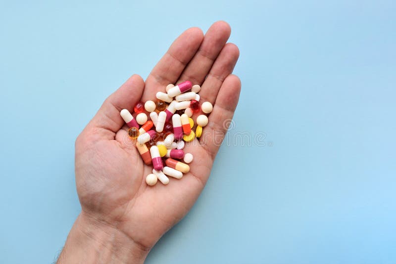 Multiple colors pills in hand on blue background. Top view